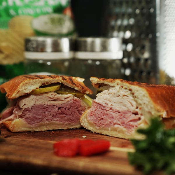 A sliced Great Wazu sandwich with ham, turkey, and pickles on a wooden board.