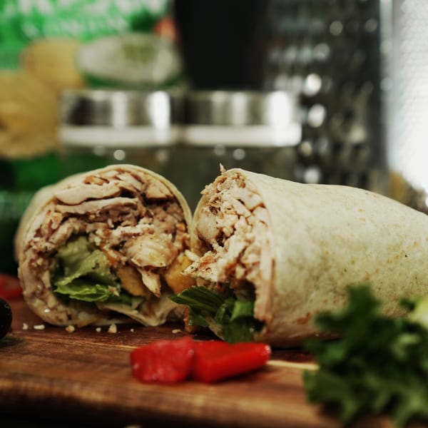 Two halves of a chicken and lettuce wrap on a wooden board with red peppers.