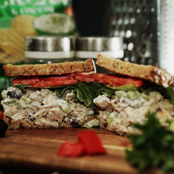A chicken salad sandwich on whole wheat bread with lettuce and tomato, cut in half on a wooden board.